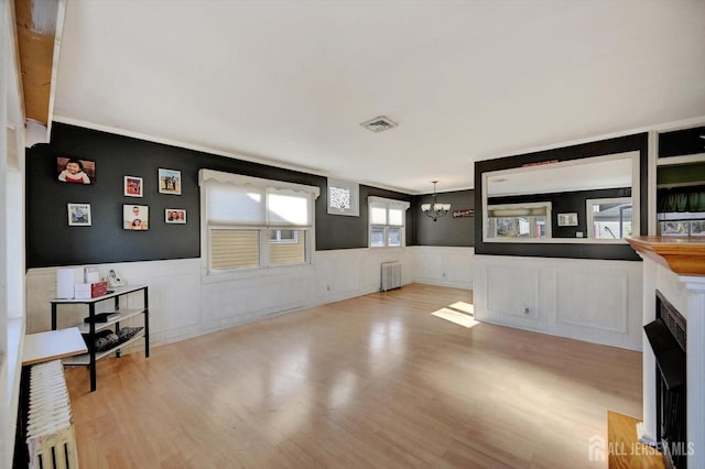 living room featuring a fireplace, radiator heating unit, light wood-type flooring, and a chandelier