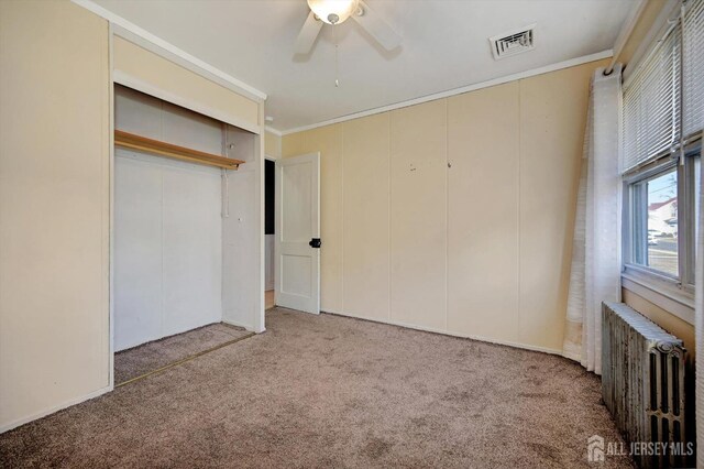 unfurnished bedroom featuring radiator, carpet flooring, ceiling fan, ornamental molding, and a closet