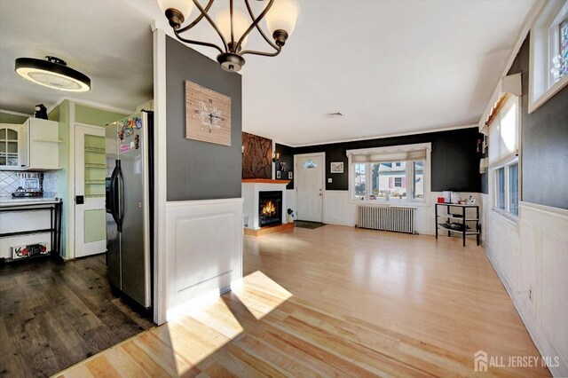 interior space featuring a notable chandelier, wood-type flooring, radiator heating unit, and crown molding