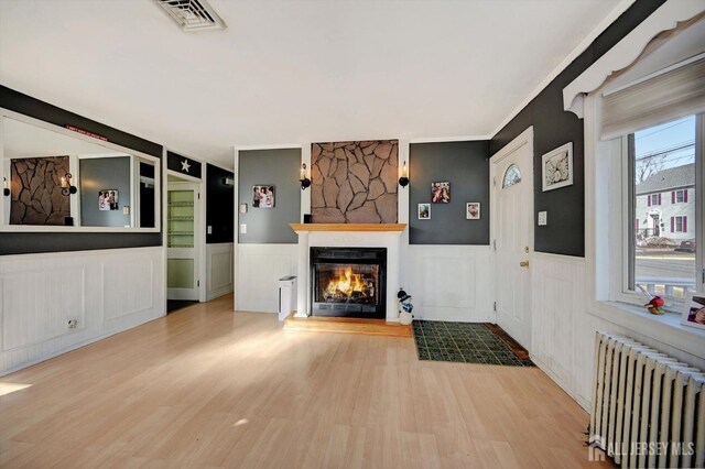 unfurnished living room featuring radiator, built in features, a fireplace, and light hardwood / wood-style flooring