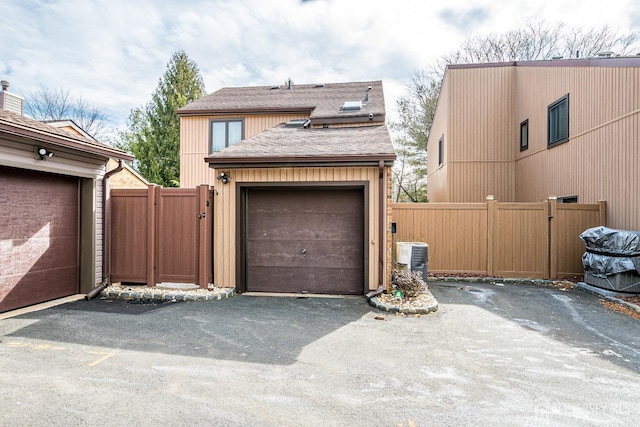 garage with aphalt driveway, a gate, fence, and central AC unit