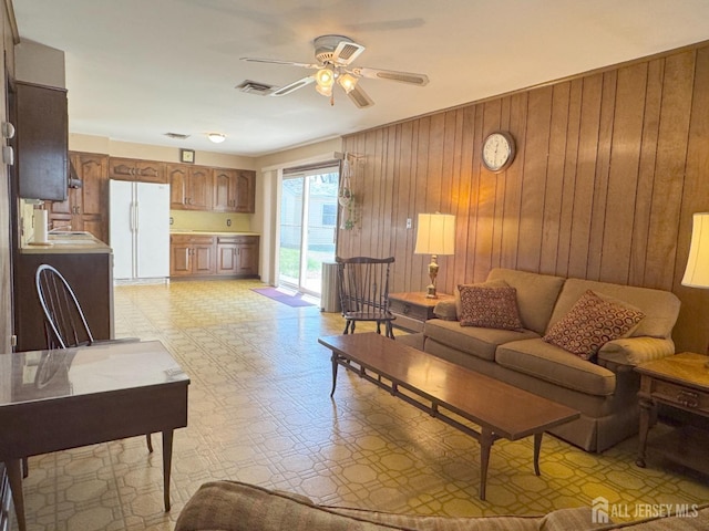 living area featuring light floors, wooden walls, and ceiling fan