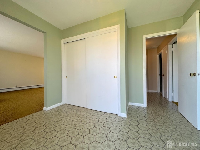 unfurnished bedroom with a closet, a baseboard radiator, baseboards, and light floors