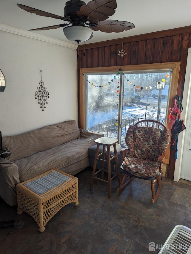 living room featuring stone finish flooring, ceiling fan, and crown molding