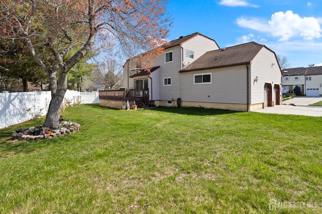 rear view of house with a garage, a yard, driveway, a deck, and fence