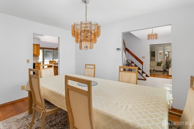 dining area featuring light wood-style floors, baseboards, a notable chandelier, and stairs