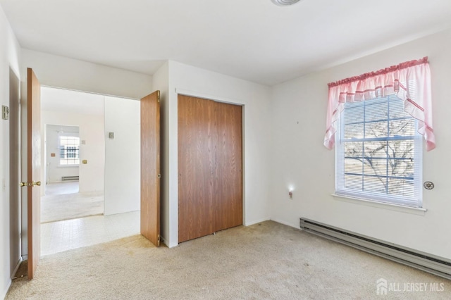 unfurnished bedroom with baseboard heating, a closet, and light colored carpet