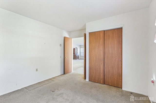 unfurnished bedroom with light colored carpet and a closet