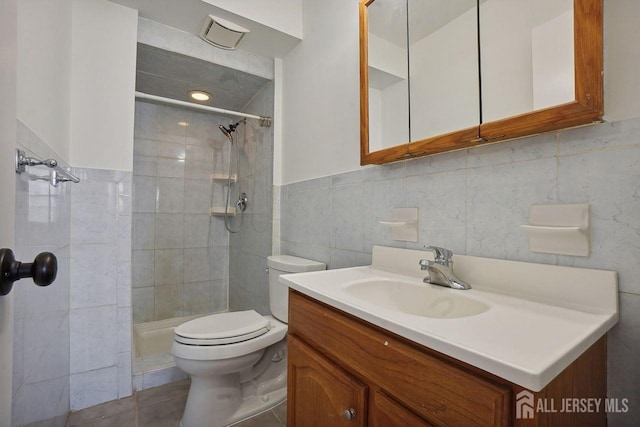 bathroom featuring tile patterned flooring, vanity, tile walls, toilet, and tiled shower