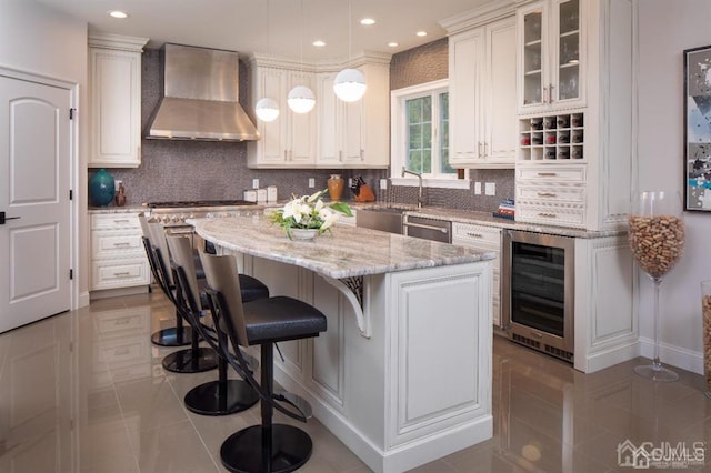 kitchen featuring white cabinets, a kitchen island, light tile patterned floors, beverage cooler, and wall chimney range hood