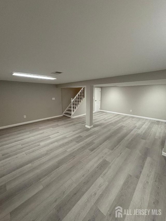 finished below grade area featuring stairs, baseboards, visible vents, and wood finished floors