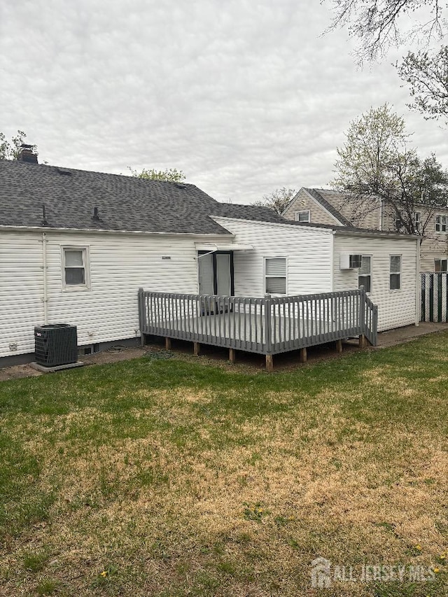 back of property featuring central air condition unit, roof with shingles, a wooden deck, and a lawn