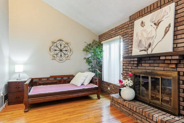 bedroom featuring light wood-type flooring, lofted ceiling, and a fireplace