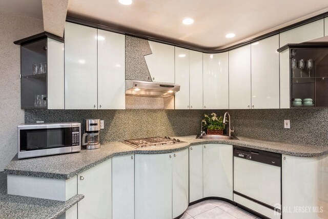 kitchen with under cabinet range hood, a sink, tasteful backsplash, appliances with stainless steel finishes, and white cabinets