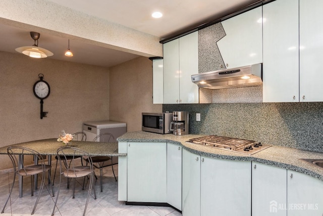 kitchen with under cabinet range hood, light countertops, decorative backsplash, white cabinets, and stainless steel appliances