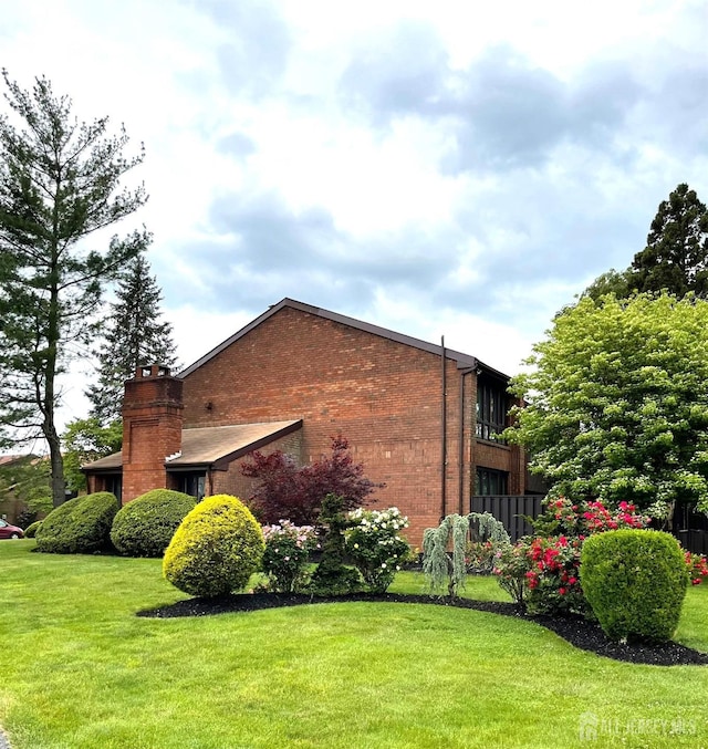 view of side of home with a yard, brick siding, and a chimney