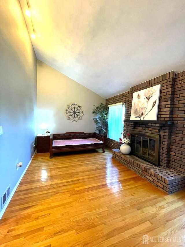 unfurnished bedroom featuring visible vents, wood finished floors, baseboards, a brick fireplace, and vaulted ceiling