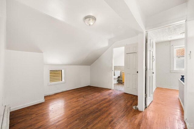 additional living space with a baseboard radiator, dark wood-type flooring, and lofted ceiling