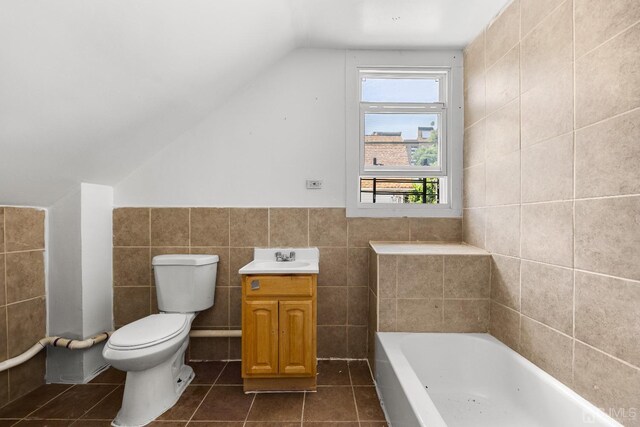 bathroom with a tub to relax in, vanity, vaulted ceiling, tile walls, and toilet