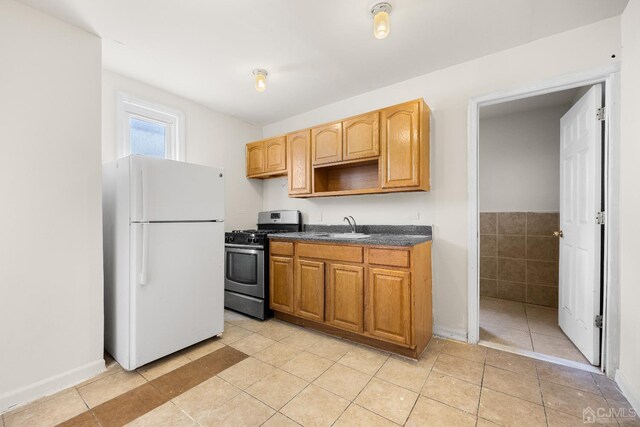 kitchen featuring white fridge, stainless steel range with gas cooktop, sink, and light tile patterned floors