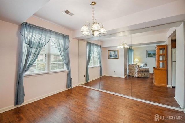 empty room featuring a notable chandelier, baseboards, visible vents, and wood finished floors