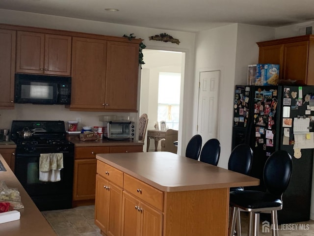 kitchen featuring a toaster, a breakfast bar, light countertops, a center island, and black appliances