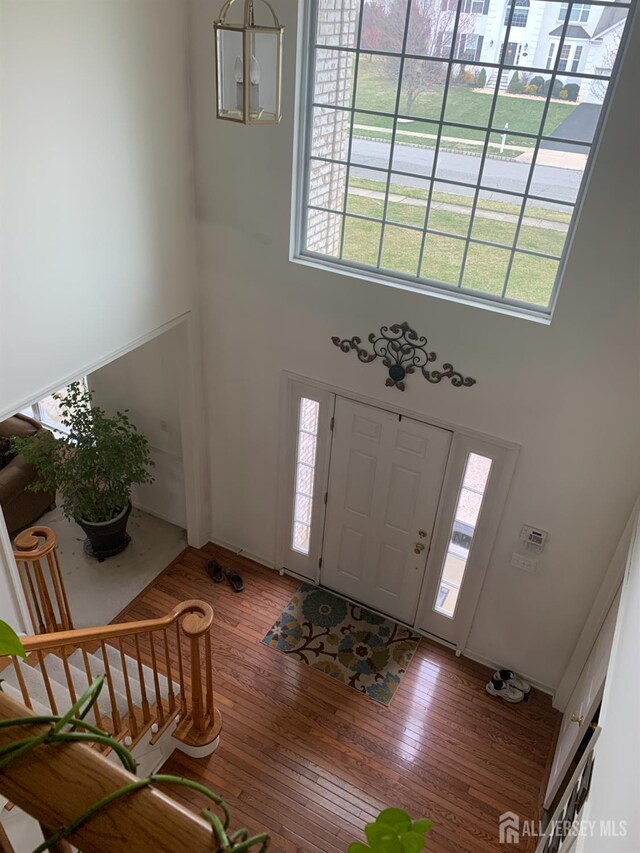 entryway featuring a notable chandelier, wood-type flooring, a towering ceiling, and a wealth of natural light