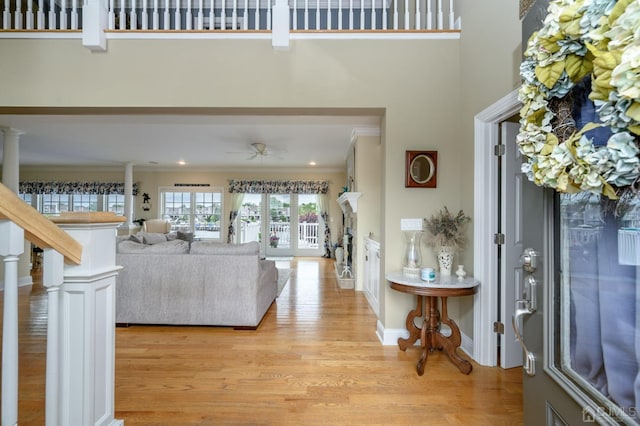 foyer entrance with a towering ceiling, ornamental molding, ceiling fan, and light wood-type flooring