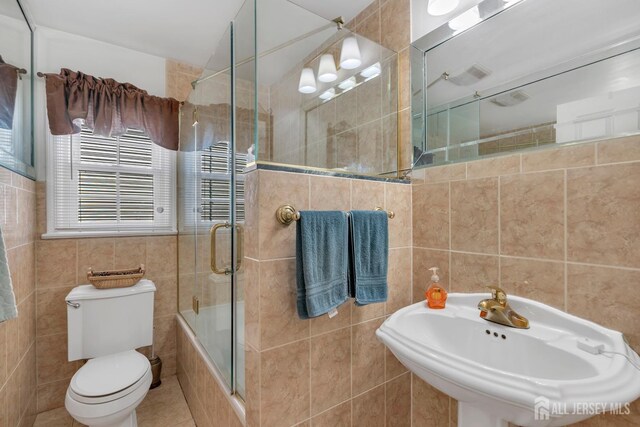 full bath with tile walls, a sink, tile patterned floors, toilet, and tiled shower / bath combo