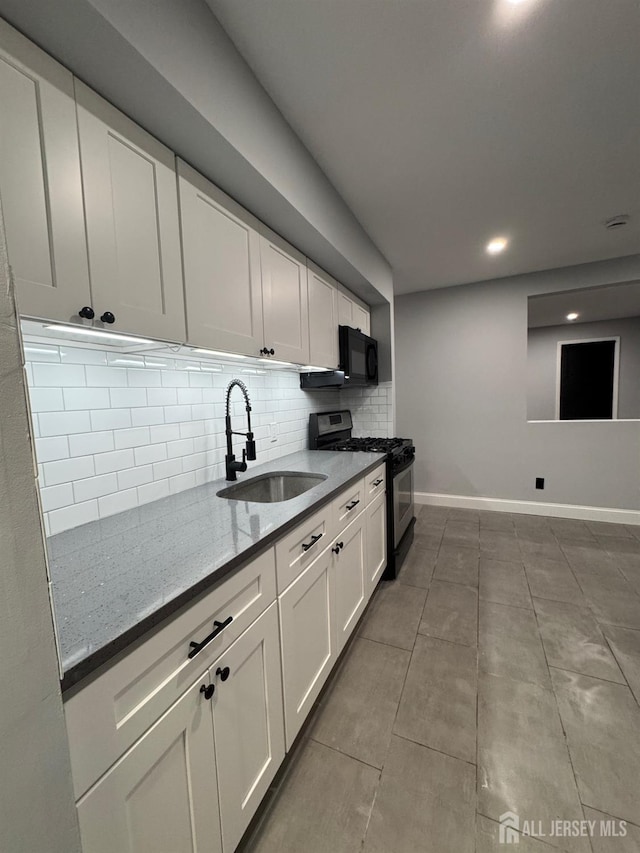 kitchen with stainless steel gas range, sink, white cabinetry, dark stone countertops, and decorative backsplash