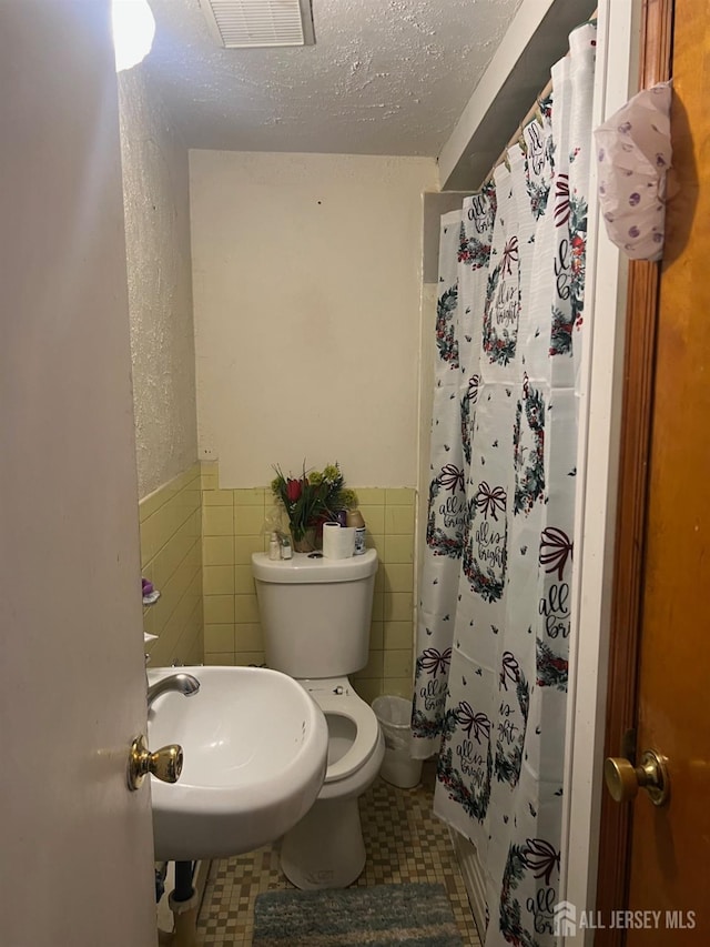 bathroom featuring toilet, sink, a textured ceiling, tile walls, and a shower with shower curtain