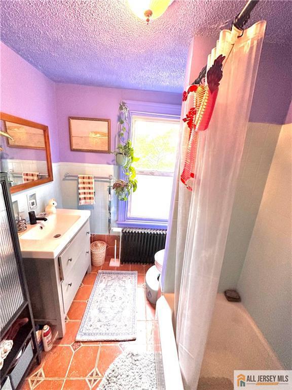 21 Alexander St, New Brunswick, NJ 08901 - bathroom with radiator heating unit, vanity, a shower with curtain, a textured ceiling, and a tub