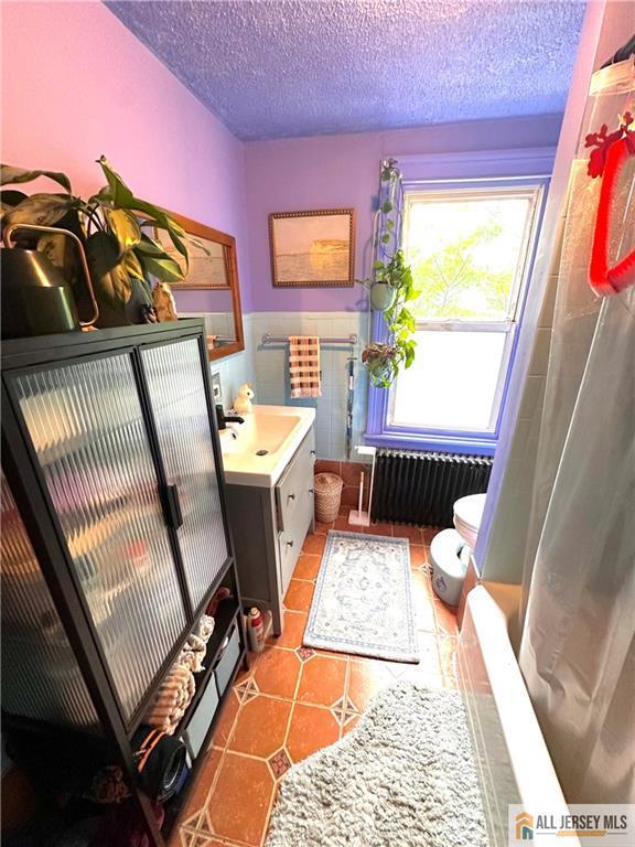 21 Alexander St, New Brunswick, NJ 08901 - bathroom featuring radiator, vanity, a textured ceiling, toilet, and a wainscoted wall