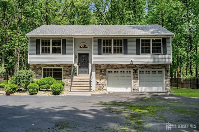 230 New Rd, South Brunswick, NJ 08852 - bi-level home with asphalt driveway, a garage, stone siding, view of wooded area, and roof with shingles