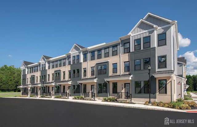 townhome / multi-family property featuring brick siding, a residential view, board and batten siding, and a standing seam roof