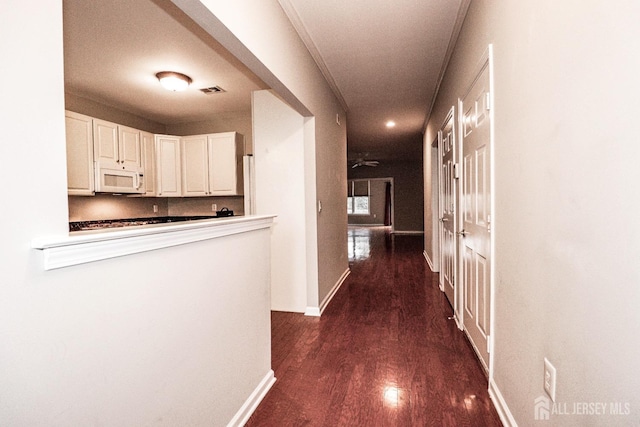 hallway with dark wood finished floors, visible vents, and baseboards