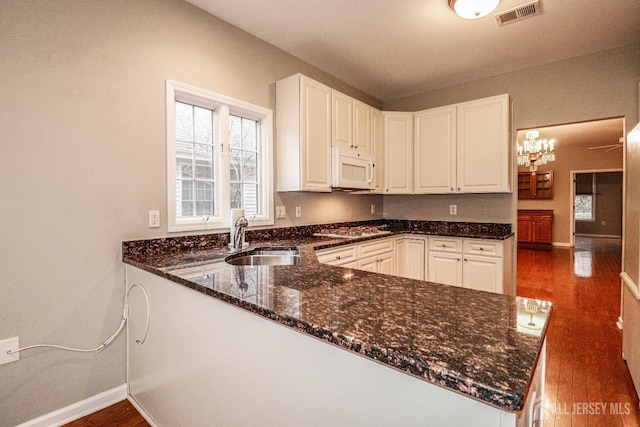 kitchen with visible vents, a sink, dark stone countertops, wood finished floors, and white microwave