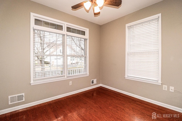 empty room featuring dark wood-style floors, visible vents, and baseboards