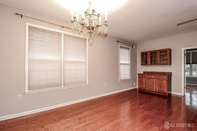 unfurnished dining area featuring a notable chandelier, dark wood-style floors, and baseboards