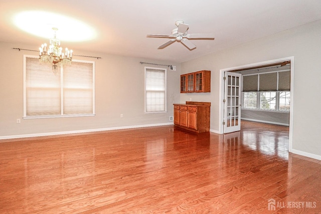 interior space with baseboards, wood finished floors, and ceiling fan with notable chandelier