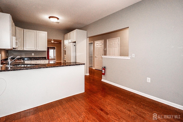 kitchen featuring white appliances, baseboards, a sink, dark wood-type flooring, and white cabinetry