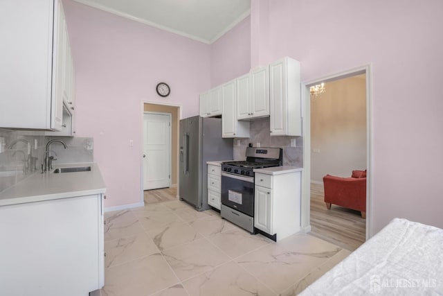 kitchen featuring a high ceiling, a sink, stainless steel appliances, white cabinets, and crown molding