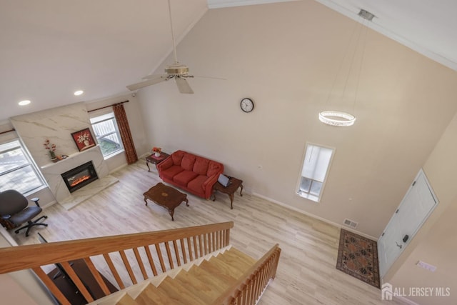 living area with visible vents, wood finished floors, a glass covered fireplace, and high vaulted ceiling