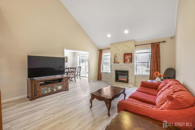 living room with a premium fireplace, recessed lighting, baseboards, high vaulted ceiling, and light wood-style floors