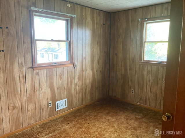 carpeted spare room with wood walls and visible vents