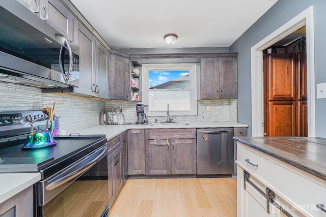 kitchen featuring decorative backsplash, appliances with stainless steel finishes, a sink, dark brown cabinets, and light wood-type flooring