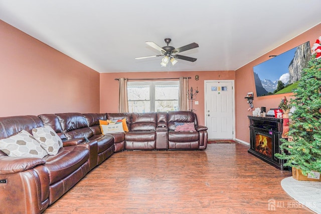 living room featuring dark wood-type flooring, a glass covered fireplace, and a ceiling fan