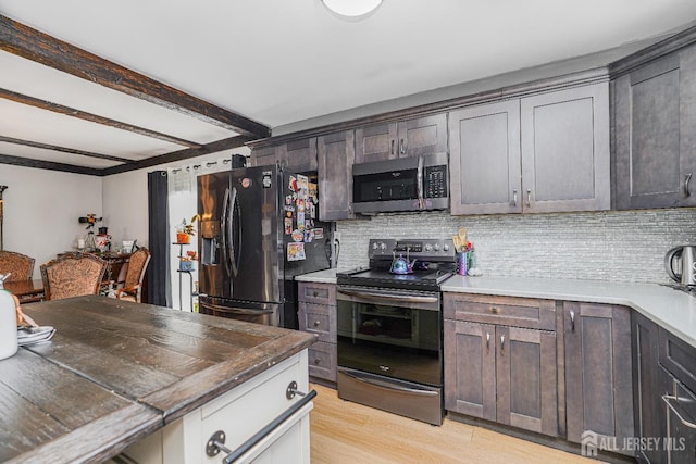 kitchen with light wood finished floors, appliances with stainless steel finishes, beamed ceiling, and tasteful backsplash