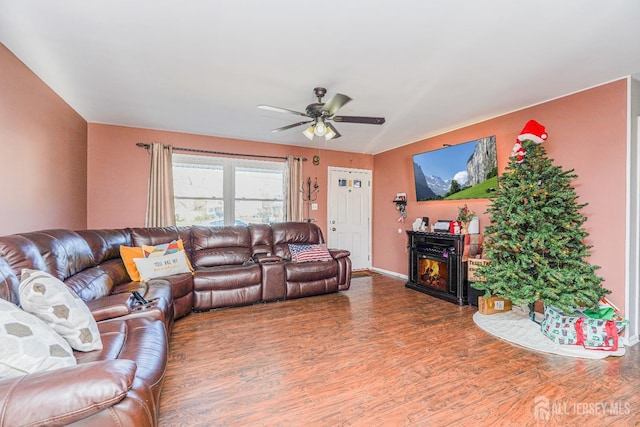 living area featuring a ceiling fan, dark wood finished floors, and a lit fireplace