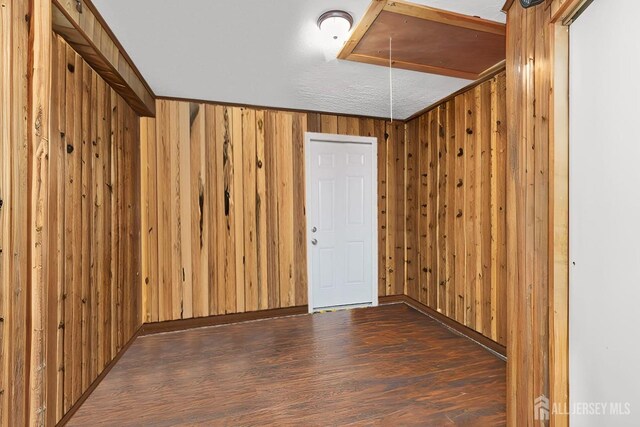 spare room with dark wood-style flooring, wood walls, and attic access